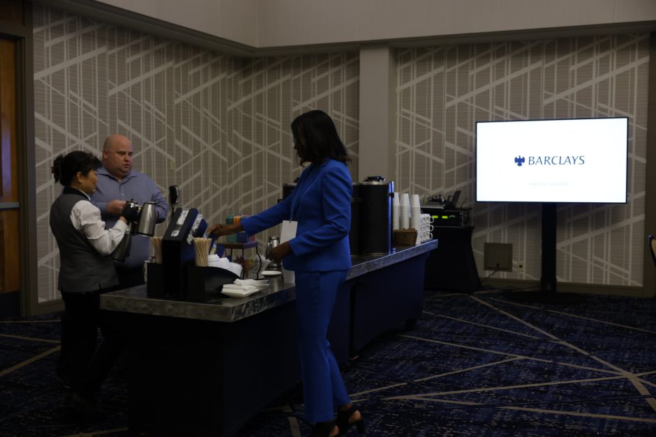 Black women in a blue suit at a refreshment table next to a screen that says Barclays. 